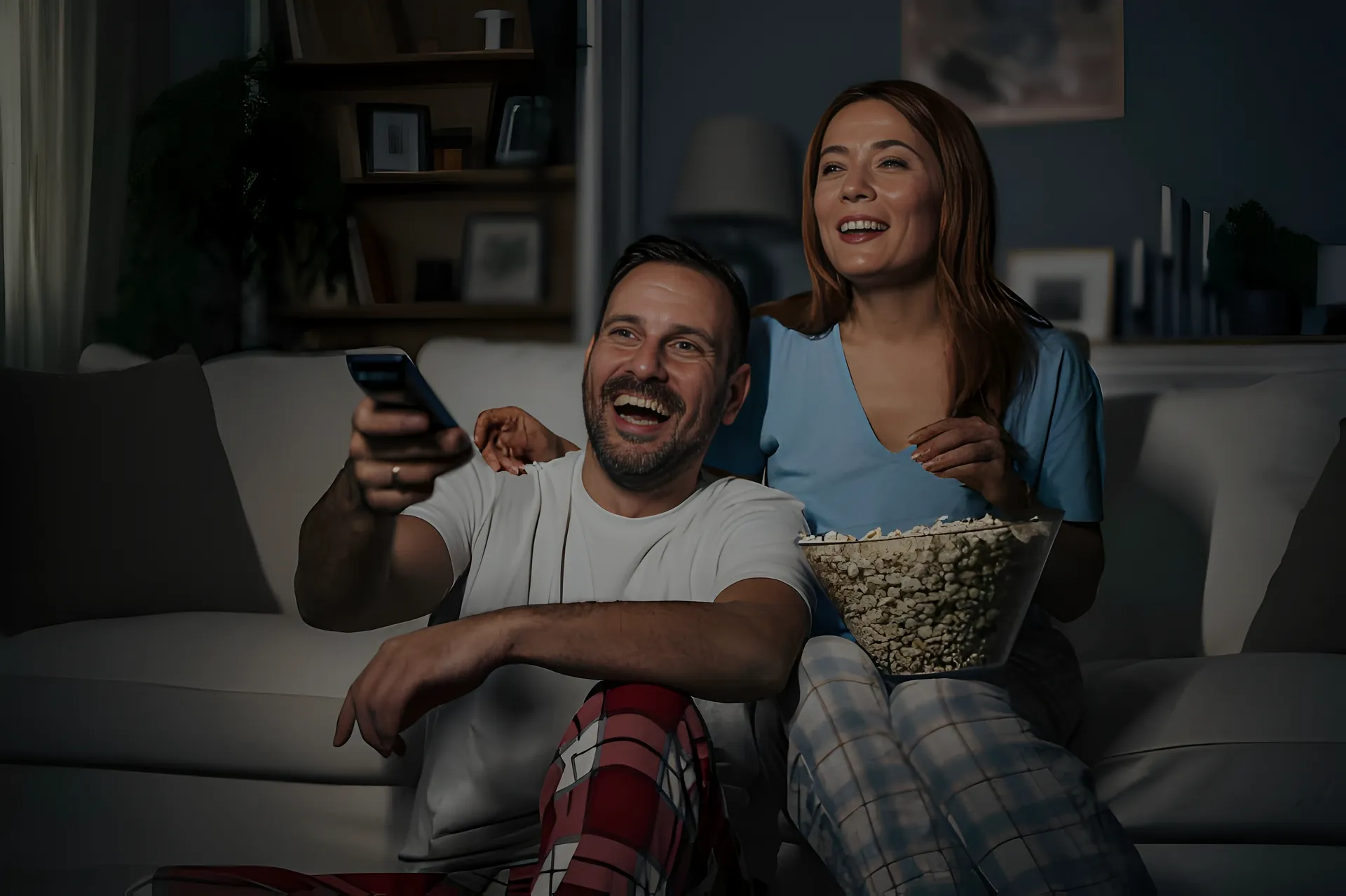 Couple relaxing on a couch at night watching Apollo Group TV IPTV with a remote and popcorn